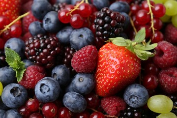 Different ripe berries and mint leaves as background, closeup