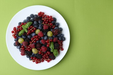 Different ripe juicy berries on plate against green background, top view. Space for text