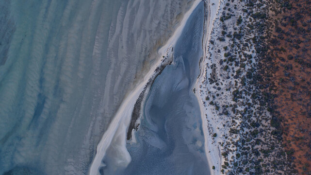 Aerial view of where the rust-colored earth meets the tranquil, rippled expanse of the sea, Shark Bay, Western Australia, Australia.