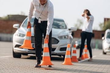 Fototapeta premium Placing the guide cones. Man instructor in the driving school and woman are outside the car