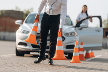 Obraz premium Placing the guide cones. Man instructor in the driving school and woman are outside the car