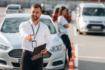 Documents in hands of a guy. Man instructor in the driving school and woman are outside the car