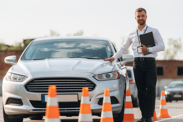 Leaning on the car. Driving school worker is outdoors