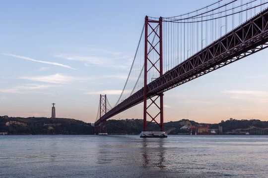 View of the vibrant red 25 de Abril Bridge stretches across the tranquil blue waters, connecting distant shores under a serene sky, Lisbon, Portugal.