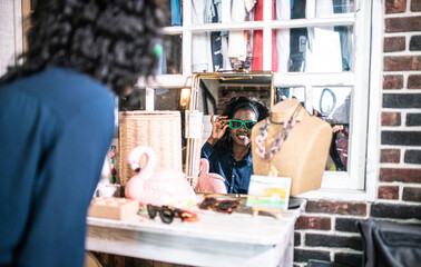 Stylish Woman With Orange Glasses Smiles At a Mirror While Shopping In a Boutique