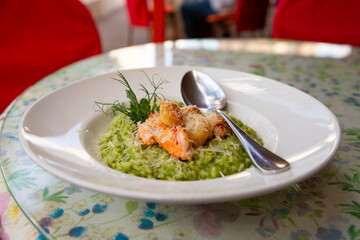 Gourmet spinach risotto with shrimp and scallop served on a floral tablecloth in a cozy restaurant setting during lunch