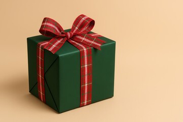 Obraz premium Green gift box with red plaid ribbon and bow on beige background, perfect for Christmas and holiday celebrations.