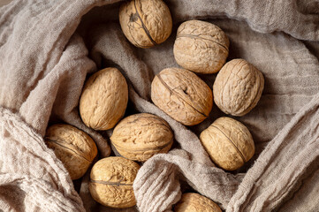 Natural close-up of unshelled walnuts placed on textured rustic fabric in warm light. Organic food still life with copy space.