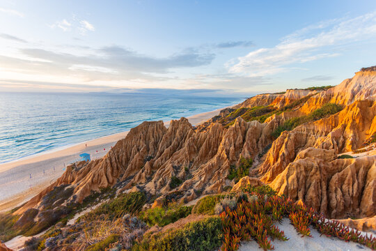 View of golden falesia cascading to meet the turquoise ocean, framing a serene beach under a pastel sky, Arriba fossil Praia da Gale Fontainhas, Setubal, Portugal.