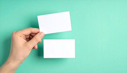 Hand holding two blank white business cards against a teal background