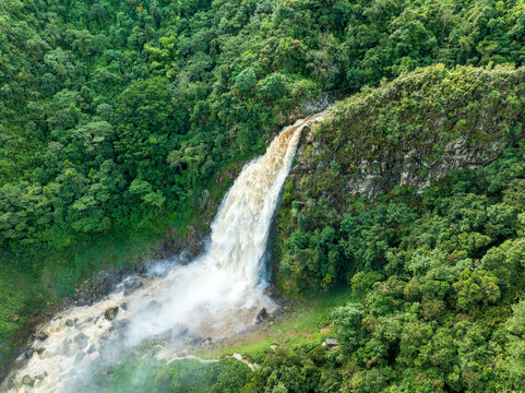 Aerial view of a powerful waterfall cascading through the dense, vibrant green rainforest, creating a striking contrast of wild energy and serene nature, Abejorral, Colombia.