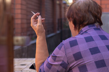 An elderly woman relaxes with a cigarette in her backyard.