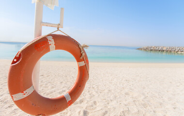 Life ring displayed on beach with clear blue water and gentle waves in bright sunlight during a peaceful afternoon