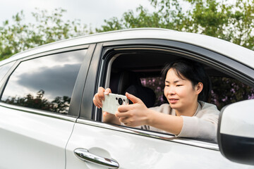 A woman is taking a selfie using her phone while sitting in a car with the window down in an...