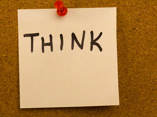 Sticky note with the word THINK pinned to cork board for motivation