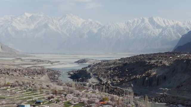 Aerial View of a Serene River Valley in Pakistan, Featuring Snow-Capped Mountains and Blooming Plum Orchards