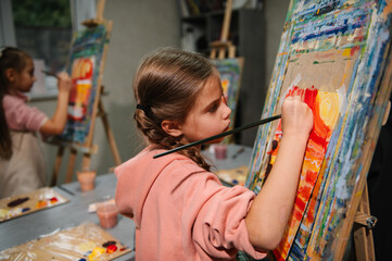 Kids draw pictures in art class. Group of school children drawing with brush landscapes on easel. Childs enjoy painting in workshop. Art lesson. Education and learning concept. Mix and combine colors.