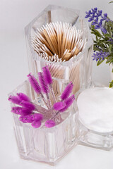 A close up of a cosmetic organizer. Cotton pads and pink eyelash and eyebrow brushes
