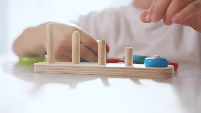 Child plays with toy r rings pyramid on table in kindergarten. Fun childhood leisure concept. The child masters fine motor lifestyle skills. Child masters fine motor skills, educational game.