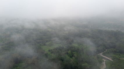 Aerial of Village in rain cloud cover tropical green mountain. Rainy season. Misty cover green forest. beautiful green village