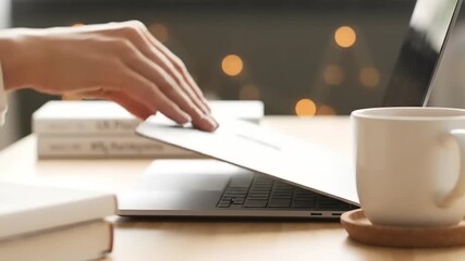 Close-up of a person's hand opening and closing a modern laptop on a wooden desk with a coffee mug and books - Powered by Adobe
