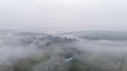 Aerial of Village in rain cloud cover tropical green mountain. Rainy season. Misty cover green forest. beautiful green village