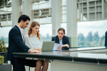 Business people working together outdoors, discussing ideas with laptop, ideal for concepts of teamwork, corporate culture, and business development at rooftop hotel.