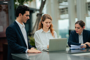 Team of executives brainstorming outdoors with laptop, showcasing business teamwork, organizational culture, and innovative planning at rooftop hotel.