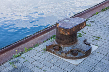 Naklejka premium Rusty metal bollard on stone pavement near harbor water at riverside dock