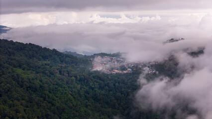Aerial of Village in rain cloud cover tropical green mountain. Rainy season. Misty cover green forest. beautiful green village
