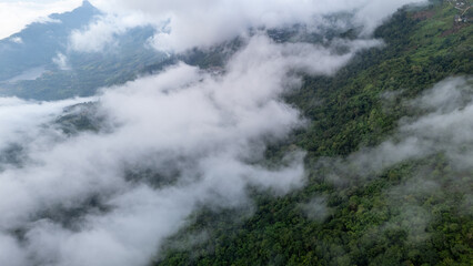 Aerial of Village in rain cloud cover tropical green mountain. Rainy season. Misty cover green forest. beautiful green village