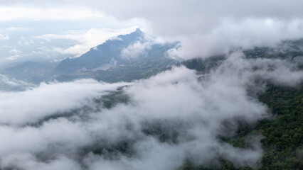 Aerial of Village in rain cloud cover tropical green mountain. Rainy season. Misty cover green forest. beautiful green village