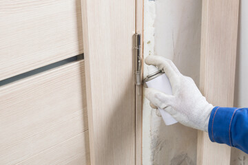 A technician wearing protective gloves lubricates a light-colored door by spraying lubricant onto...