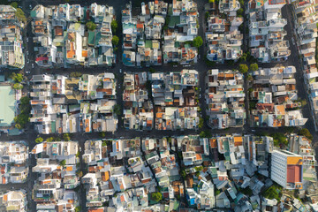 A high angle shows densely populated residential and commercial buildings with colorful roofs situated along a grid of streets in Ho Chi Minh City during the day