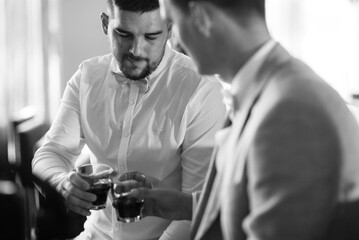 portrait of a groom in a suit and white bow tie sitting in a hotel lobby with a friend