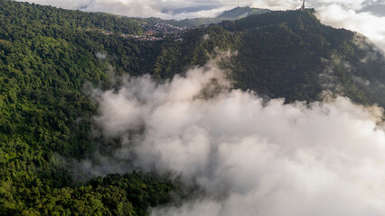 Aerial of Village in rain cloud cover tropical green mountain. Rainy season. Misty cover green forest. beautiful green village