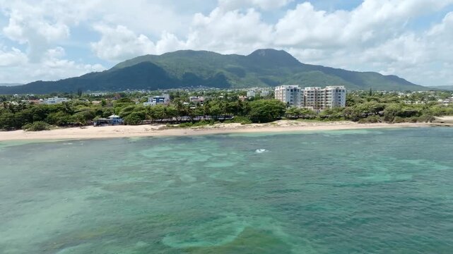 Aerial wide shot showing Sandy beach of puerto plata in Dominican Republic. Waterfront houses and apartment compel hotel. Green mountains in distance.