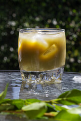 Vibrant iced matcha in clear glass on outdoor glass table. Sunlight highlights cool, refreshing drink and lush green leaves. Perfect summer vibe.