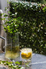 Iced matcha latte on a glass table with green leaves, on a sunny outdoor patio. Vibrant green and serene ambiance.