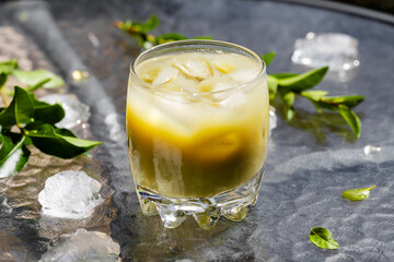 A vibrant iced matcha latte with ice cubes and fresh green leaves rests on a textured glass table. This cool, creamy, and energizing green tea beverage offers a refreshing escape.
