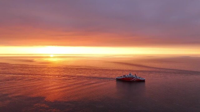 List auf Sylt, Germany - 09 September 2025: Aerial view of a red and white RoRo ship sailing on the sea as the sun sets with golden and orange hues.