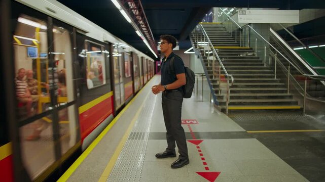 A man waits for the train to stop standing on the subway platform. He enters the subway by passing through the turnstile and waits for the train standing on the platform.