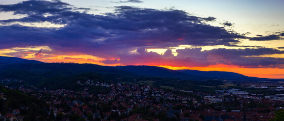 Breathtaking Panoramic Sunset Paints A Vivid Palette Of Red And Purple Across The Sky Over A Town And Forested Hills