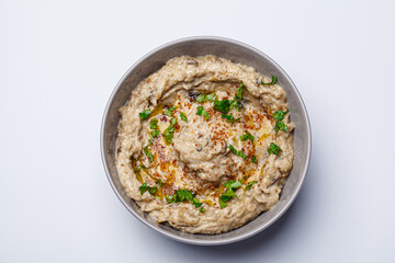 Baba ganoush - spread of baked eggplant with tahini and spices in gray bowl on white background.