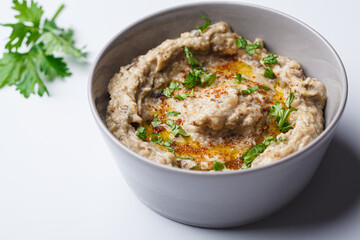 Baba ganoush - spread of baked eggplant with tahini and spices in gray bowl on white background.