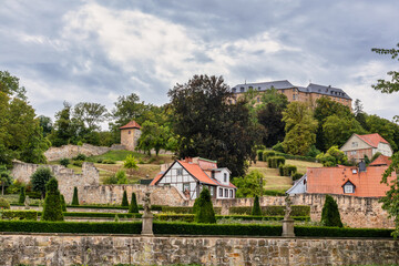 Majestic Stone Castle And Its Walls Stand Atop A Hill Overlooking A Formal Garden With Neatly Trimmed Hedges And Stone Statues