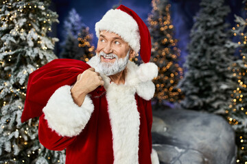 Cheerful Santa Claus in a red suit near festive fir trees during winter season