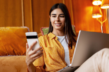 Woman using smartphone and laptop multitasking at home