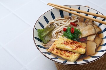 Tasty ramen with king oyster (eryngii) mushrooms in bowl on white tiled table, closeup
