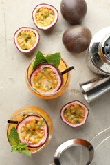 Tasty passion fruit drink with mint in glasses, fresh fruits and bartender's tools on gray textured table, flat lay